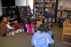 two men read to a group of children and parents