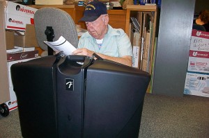 man sitting behind large black electronic equipment case, reading an instruction manual