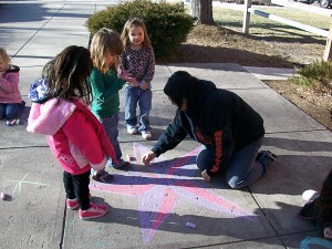 teacher draws colorful star with chalk on sidewalk while three children look on