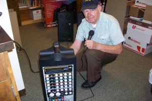 man holding microphone kneels next to portable amplifier